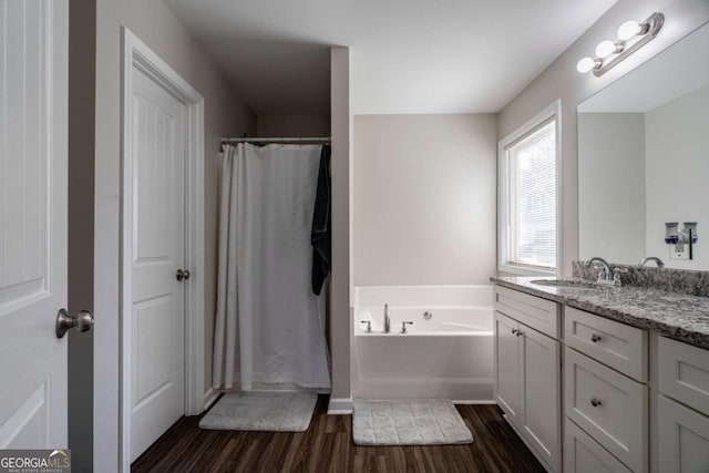 full bath featuring vanity, a garden tub, curtained shower, and wood finished floors