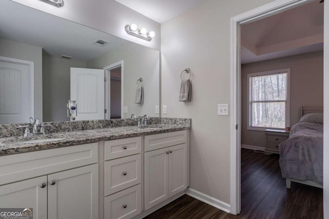 ensuite bathroom with visible vents, wood finished floors, baseboards, and a sink