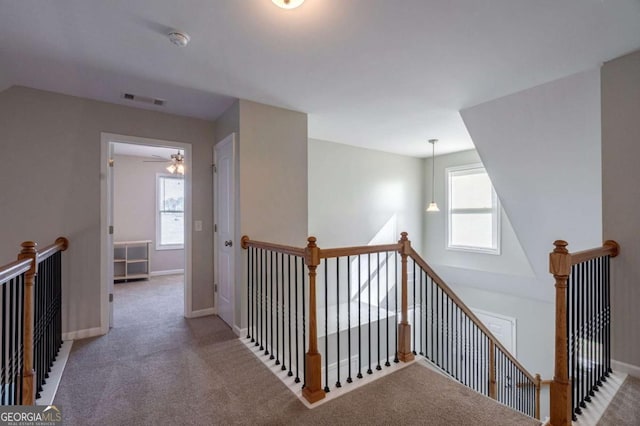 corridor featuring an upstairs landing, visible vents, plenty of natural light, and carpet floors