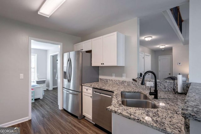 kitchen featuring dark wood-type flooring, light stone counters, white cabinets, stainless steel appliances, and a sink