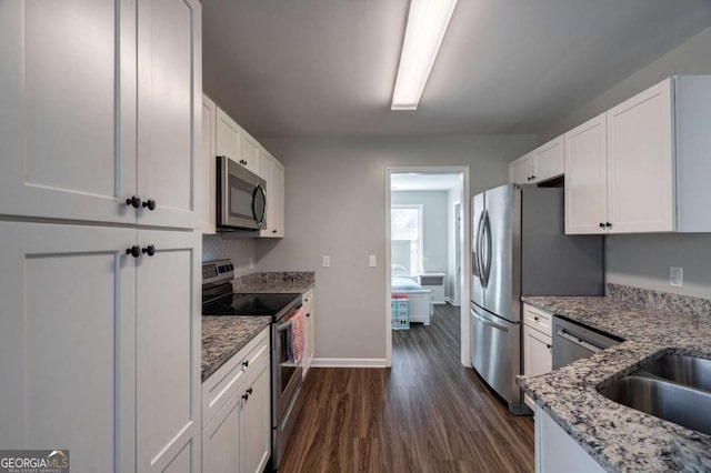 kitchen featuring light stone counters, dark wood-style floors, stainless steel appliances, white cabinets, and baseboards