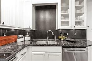 kitchen with dark stone countertops, white cabinets, dishwasher, and a sink