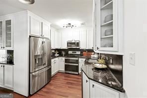 kitchen with dark countertops, glass insert cabinets, dark wood-type flooring, appliances with stainless steel finishes, and white cabinetry