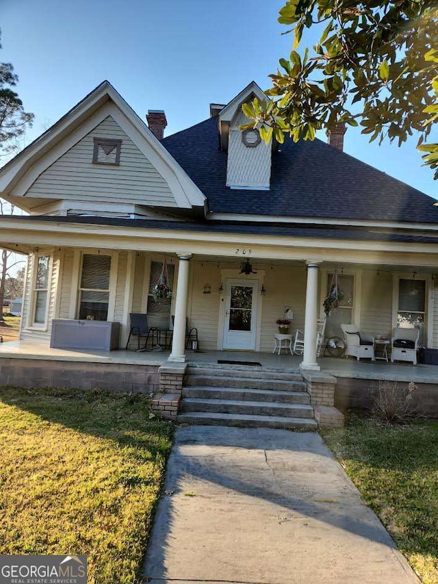 view of front of property with covered porch, a chimney, and a shingled roof