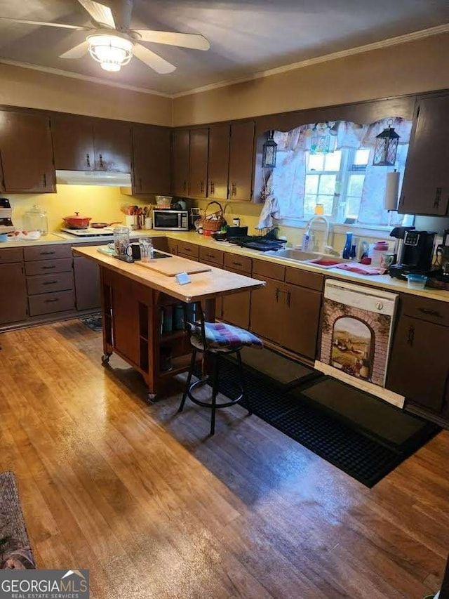 kitchen featuring ornamental molding, light wood-style flooring, stainless steel microwave, white dishwasher, and light countertops