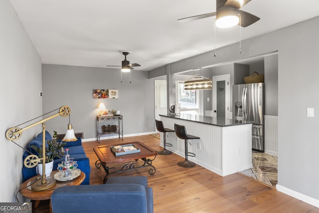 living area featuring baseboards, light wood-type flooring, and ceiling fan