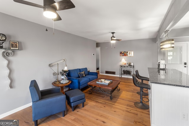 living room with ceiling fan, light wood-style floors, visible vents, and baseboards