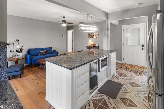 kitchen with beverage cooler, dark stone counters, freestanding refrigerator, white cabinets, and open floor plan