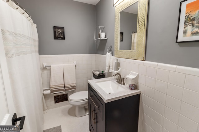 bathroom featuring tile patterned floors, visible vents, toilet, tile walls, and wainscoting