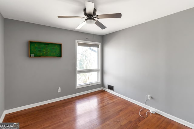 spare room featuring ceiling fan, visible vents, baseboards, and wood finished floors