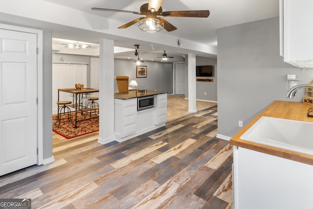 kitchen featuring baseboards, dark wood-style flooring, a sink, white cabinets, and stainless steel microwave