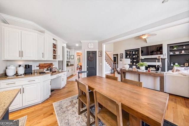 dining room with built in shelves, a ceiling fan, ornamental molding, stairs, and light wood-style floors