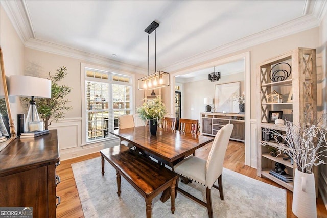 dining room with a decorative wall, light wood-style floors, wainscoting, and crown molding