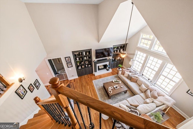 living room with baseboards, wood finished floors, a fireplace with raised hearth, and a towering ceiling