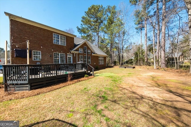 rear view of house with a yard, brick siding, and a deck