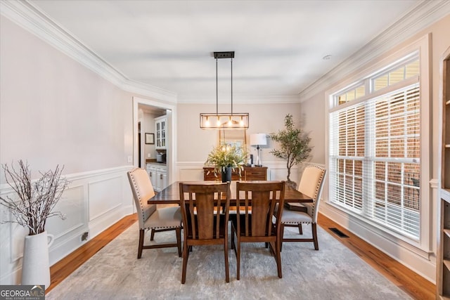 dining space with visible vents, ornamental molding, wood finished floors, wainscoting, and a decorative wall