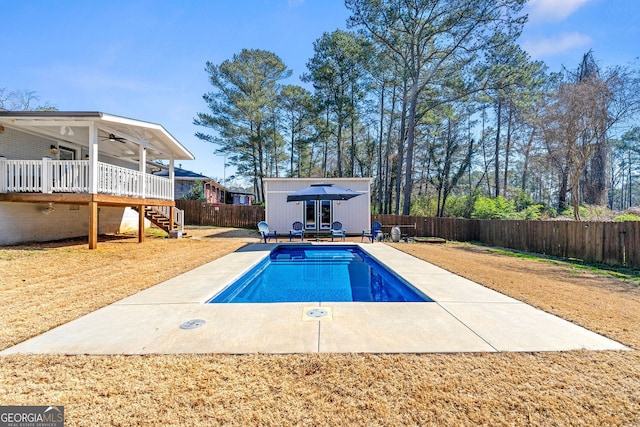 view of swimming pool with an outbuilding, a deck, a ceiling fan, a fenced backyard, and stairway