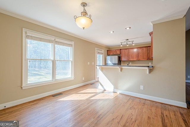 kitchen with visible vents, a breakfast bar, ornamental molding, brown cabinets, and refrigerator