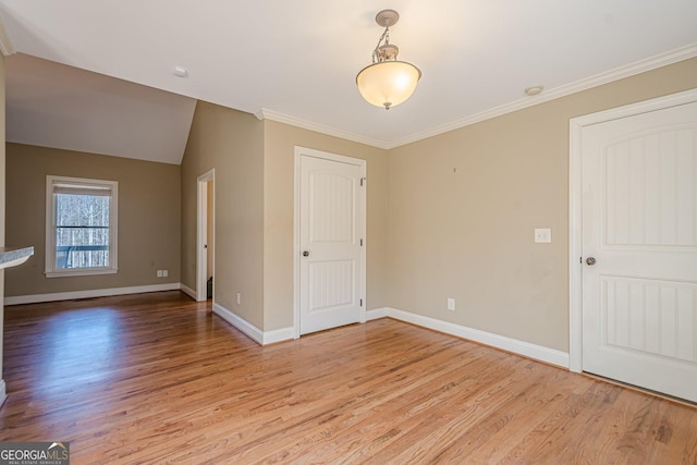 spare room featuring baseboards, light wood-style floors, ornamental molding, and vaulted ceiling