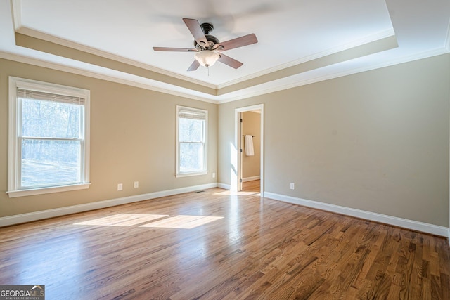 empty room with plenty of natural light, a tray ceiling, and wood finished floors