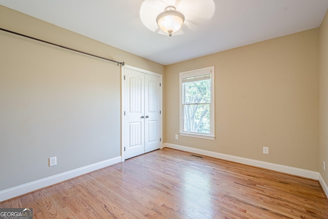 unfurnished bedroom with a closet, visible vents, baseboards, and wood finished floors