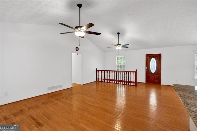 unfurnished living room featuring hardwood / wood-style floors, visible vents, lofted ceiling, ceiling fan, and a textured ceiling