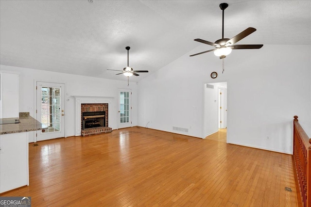 unfurnished living room with visible vents, a brick fireplace, a textured ceiling, and light wood-style floors