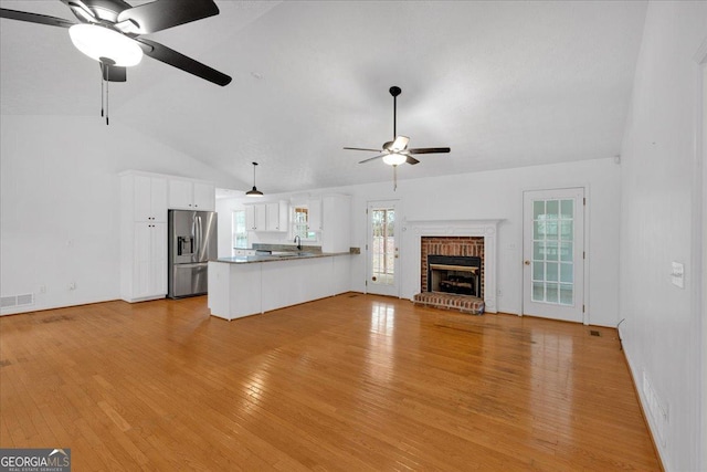 unfurnished living room featuring a ceiling fan, visible vents, lofted ceiling, light wood-style flooring, and a brick fireplace