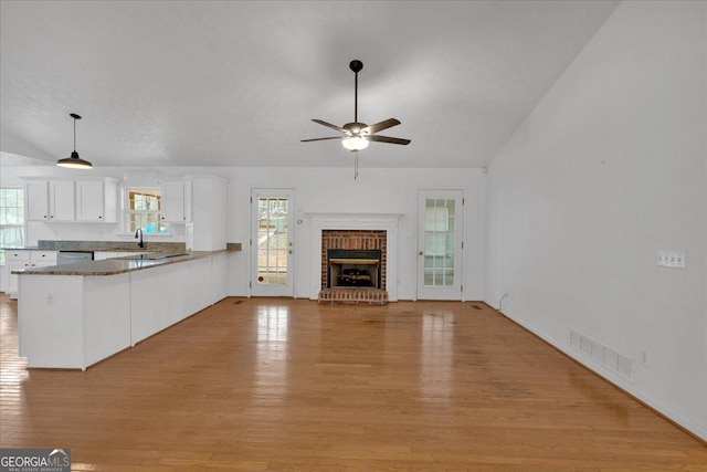 unfurnished living room with vaulted ceiling, a fireplace, visible vents, and light wood-type flooring