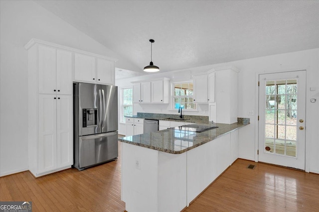 kitchen with dark stone counters, a peninsula, a sink, stainless steel appliances, and vaulted ceiling