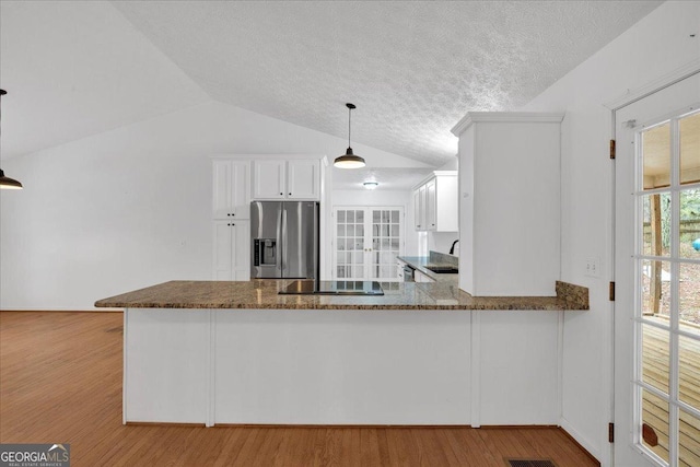 kitchen featuring wood finished floors, lofted ceiling, a peninsula, stainless steel fridge with ice dispenser, and white cabinetry