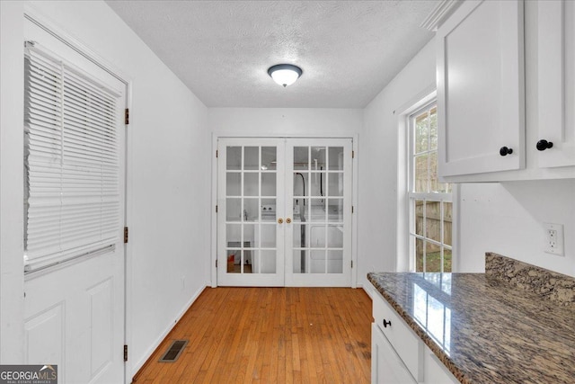 interior space with light wood-type flooring, visible vents, a textured ceiling, french doors, and baseboards