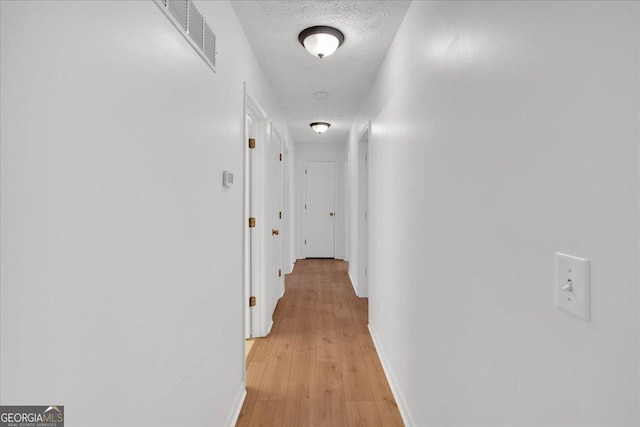 hall with baseboards, visible vents, a textured ceiling, and light wood-style floors