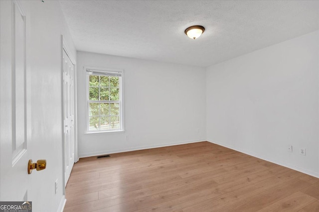 unfurnished room with visible vents, light wood-style flooring, a textured ceiling, and baseboards