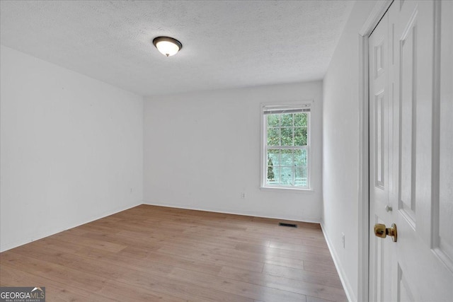 empty room with visible vents, a textured ceiling, and light wood finished floors