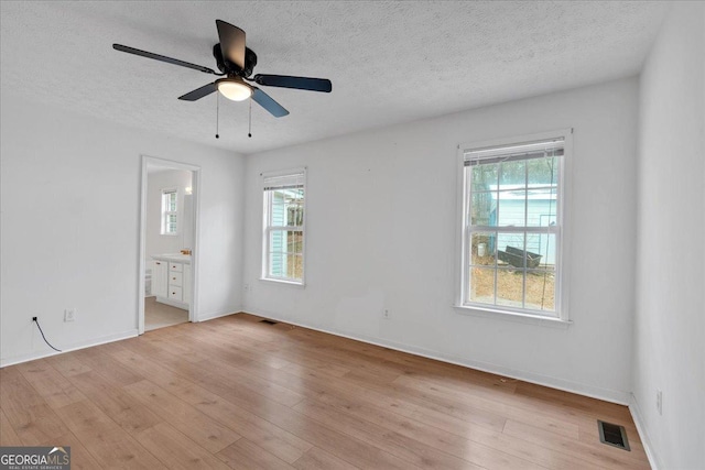 unfurnished bedroom featuring visible vents, multiple windows, a textured ceiling, and light wood-style floors