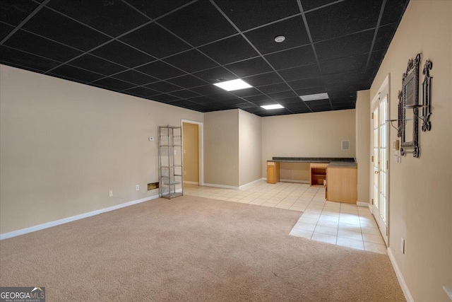 empty room with light tile patterned floors, a drop ceiling, baseboards, and light colored carpet