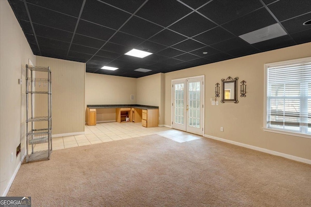 empty room featuring light carpet, french doors, a paneled ceiling, and a wealth of natural light