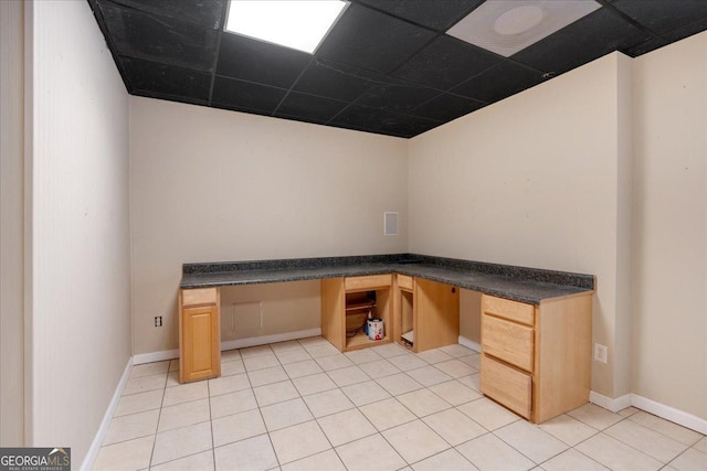 unfurnished office with light tile patterned floors, a paneled ceiling, built in desk, and baseboards