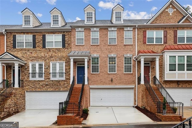 multi unit property featuring an attached garage, concrete driveway, stairway, and brick siding