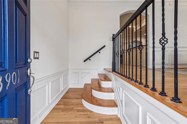 entrance foyer featuring light wood-type flooring, stairway, arched walkways, crown molding, and a decorative wall