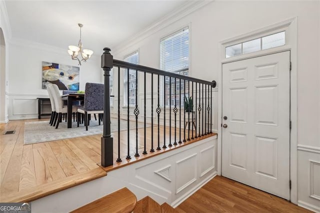 entryway featuring a decorative wall, hardwood / wood-style flooring, crown molding, and a chandelier