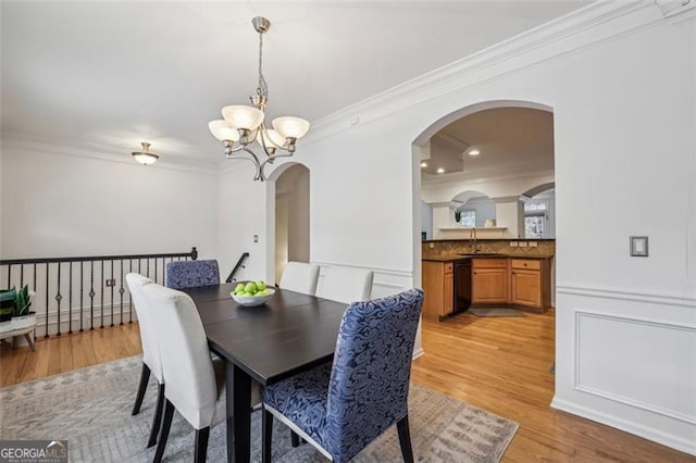 dining space featuring arched walkways, ornamental molding, a chandelier, and light wood-style floors