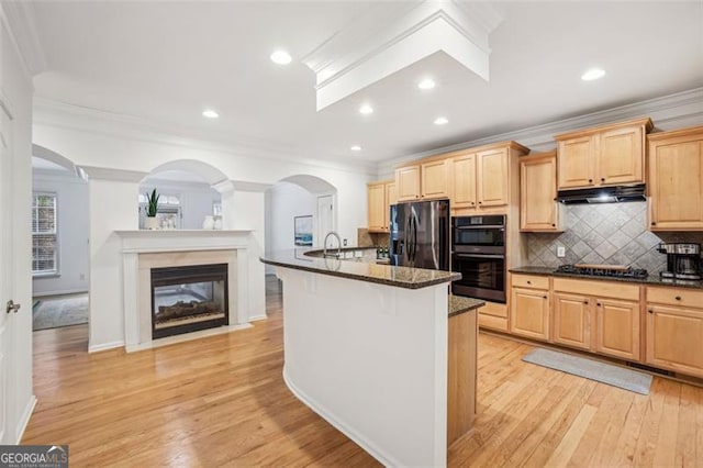 kitchen featuring light wood-type flooring, black appliances, light brown cabinetry, under cabinet range hood, and dark stone countertops