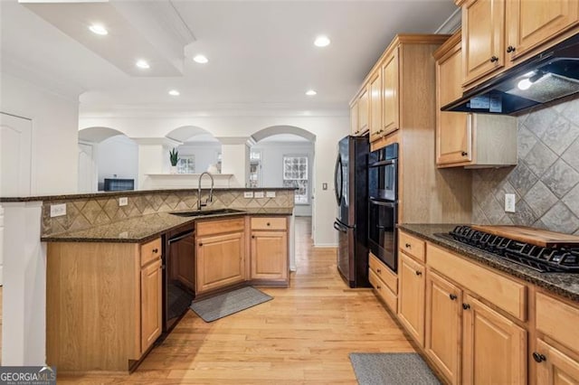 kitchen with dark stone countertops, arched walkways, a sink, black appliances, and under cabinet range hood