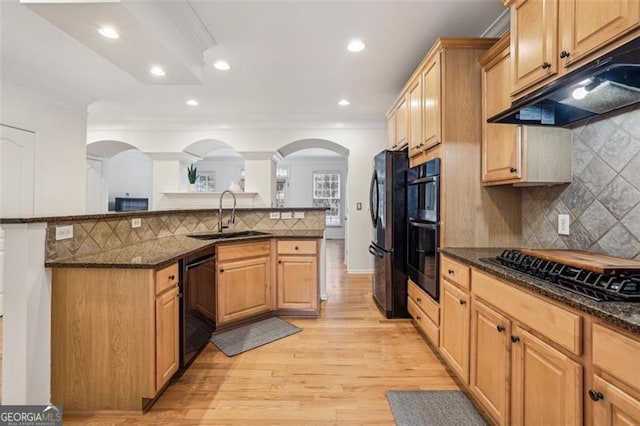 kitchen featuring under cabinet range hood, dark stone counters, a sink, arched walkways, and black appliances