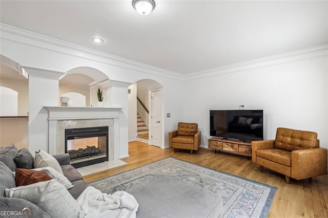 living area with crown molding, arched walkways, a tiled fireplace, and wood finished floors