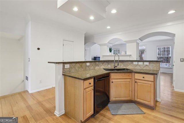 kitchen featuring arched walkways, backsplash, black dishwasher, and a sink