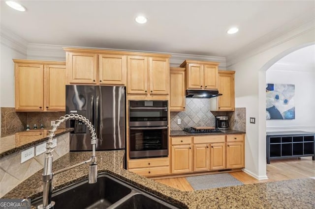 kitchen featuring arched walkways, stainless steel appliances, dark stone counters, and light brown cabinetry