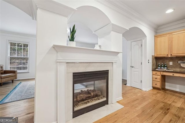 interior space with decorative backsplash, ornamental molding, a fireplace, and wood finished floors